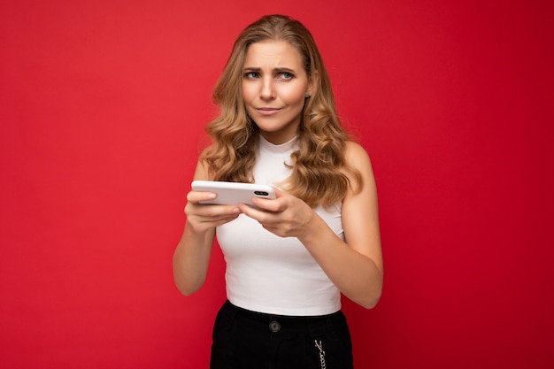 geconcentreerde mooie jonge blonde vrouw die wit t-shirt draagt dat op rood wordt geïsoleerd