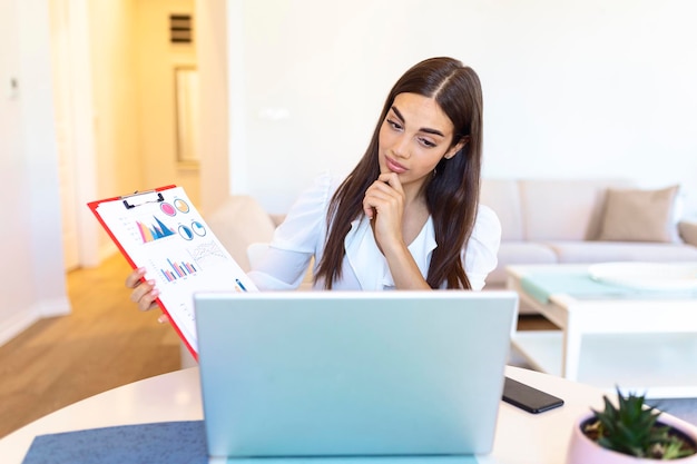 Geconcentreerde onderneemster die grafieken en grafieken op videogesprek online voorstelt. Jonge zakenvrouw met telefonische vergadering met client op laptop. Closeup zakenvrouw werkende laptopcomputer binnen.