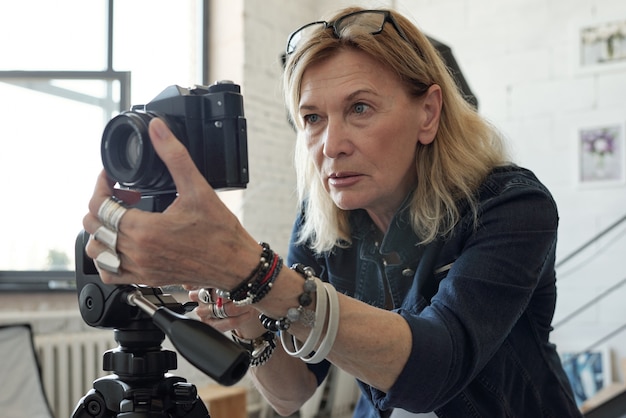 Geconcentreerde rijpe dame met blond haar cameralens aanpassen tijdens het nemen van foto in moderne studio