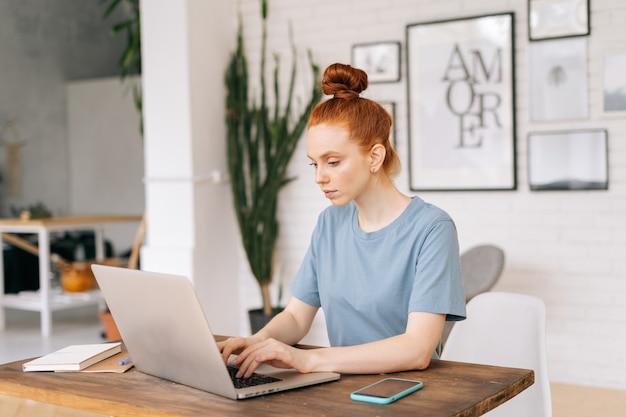 Geconcentreerde roodharige jonge vrouw werkt op moderne laptopcomputer