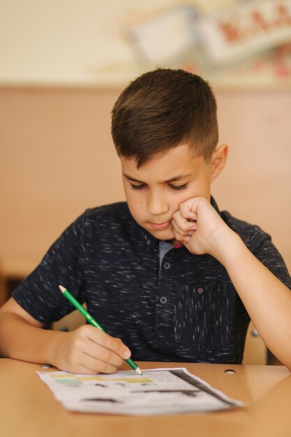 Geconcentreerde schooljongen die aan bureau zit en in werkboek schrijft. Leren concept