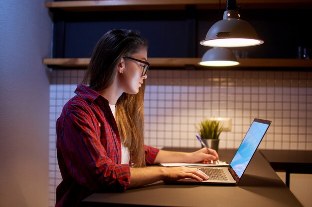 Geconcentreerde studente in glazen kijken naar online webinarcursussen en communiceren via videovergadering. e leren en examenvoorbereiding met behulp van een laptop thuis