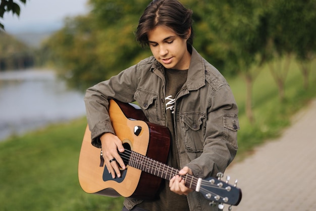 Geconcentreerde tienermuzikant die akoestische gitaar buiten speelt, knappe jongen houdt van misuc