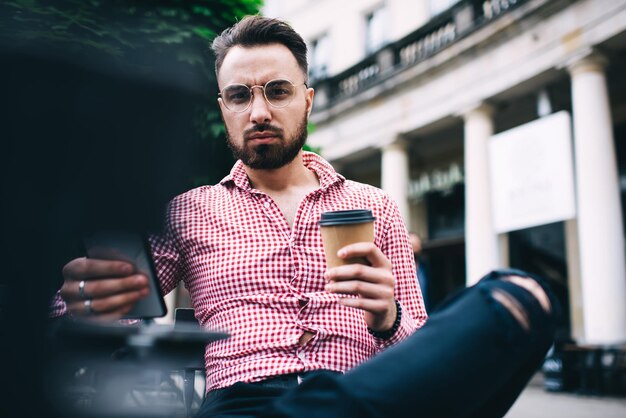 Geconcentreerde trendy mannen die mobiel op straat browsen