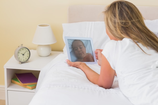 Geconcentreerde vrouw die een tabletpc met behulp van die op haar bed ligt