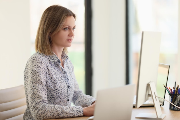 Geconcentreerde vrouw kijkt naar computer- en laptopschermen en houdt statistieken in de gaten waar blonde manager bij zit