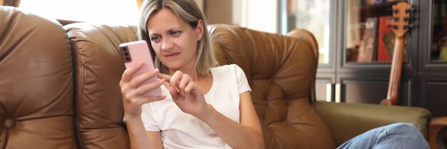 Geconcentreerde vrouw kijkt naar het scherm van haar telefoon terwijl ze thuis op de bank zit