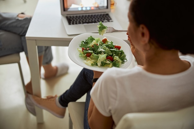 Foto geconcentreerde vrouwelijke persoon die tijdens het eten naar het scherm van haar laptop kijkt