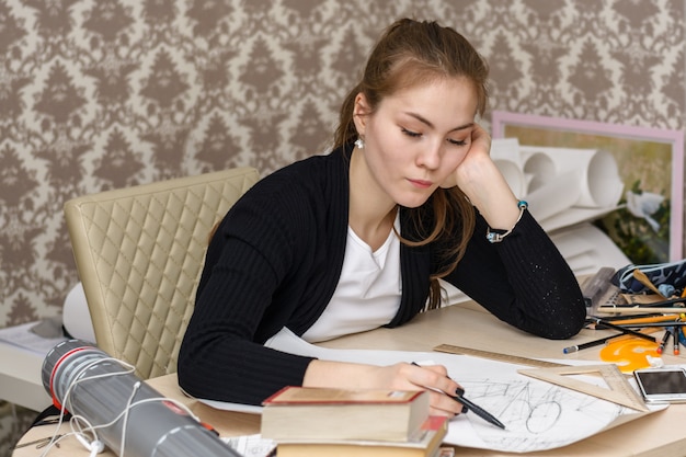 Geconcentreerde vrouwelijke student architect schetsen tekenen op het witte doek zit voor het bureaublad.