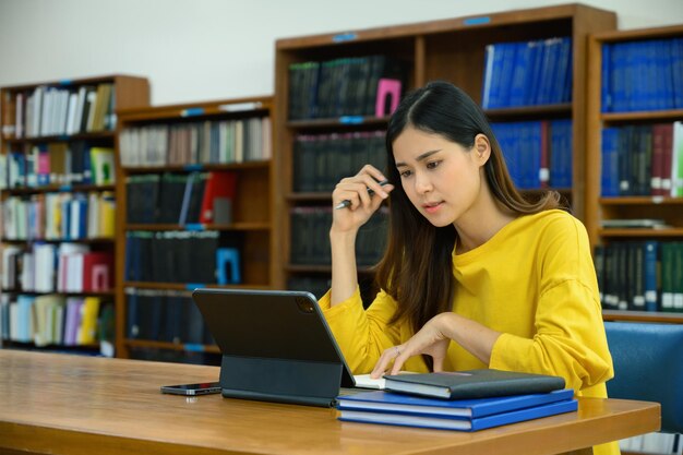 Geconcentreerde vrouwelijke universiteitsstudent die onderzoek doet naar digitale tabletleerlessen ter voorbereiding op examens in de bibliotheek
