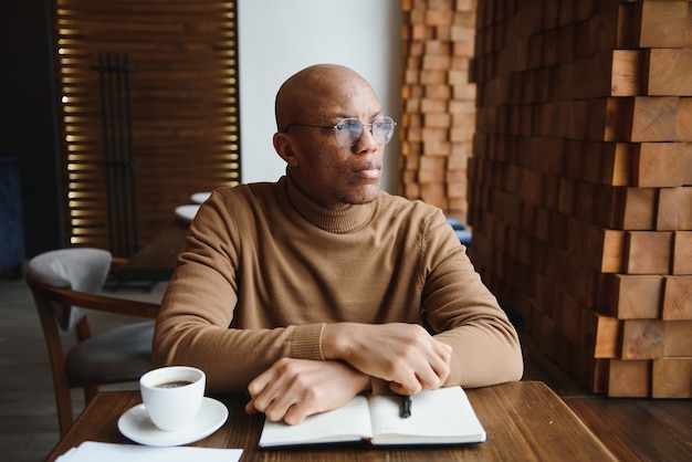 Geconcentreerde zwarte mannelijke ondernemer leest papieren documenten in café met koffie bij het raam.