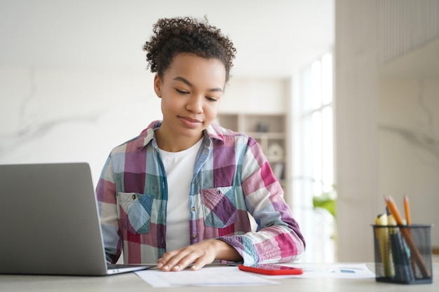 Foto geconcentreerde zwarte meisjes studeren met een laptop en notities in een heldere thuisomgeving