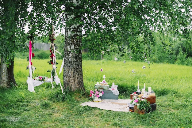 Gedecoreerde ruimte voor de bruiloft met schommels, bloemen en decoraties buiten onder een boom