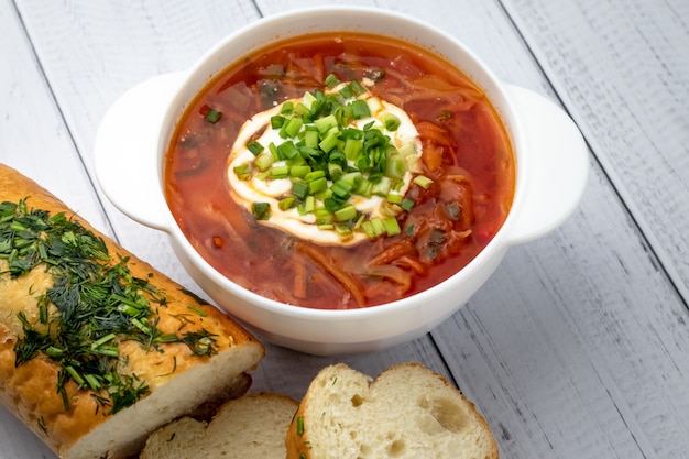 Gedeelte hete bietensoep met zure room en greens. Oekraïense traditionele schotel, Russische keuken. Rode borscht in witte kom op houten plankenachtergrond.