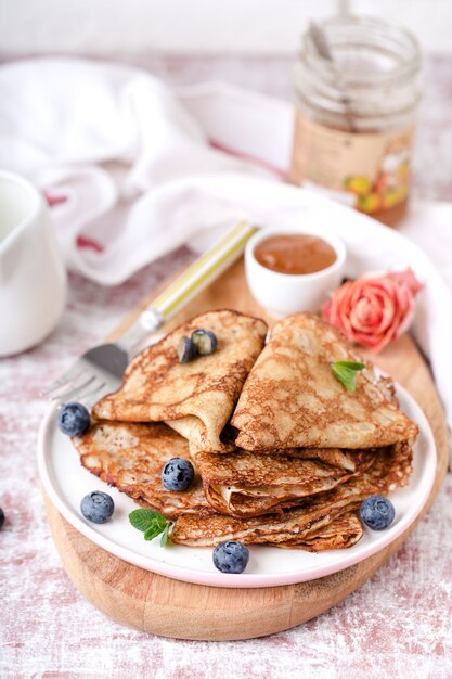 Gedeelte van gebakken pannenkoeken met honing en bosbessen, in een bord, op een houten bord, op tafel. Verticaal formaat