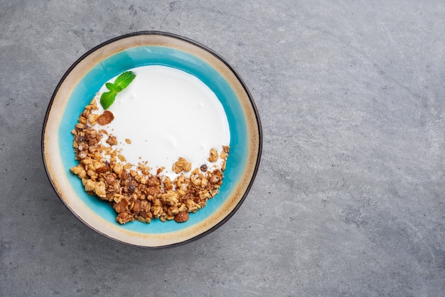 Gedeelte van natuurlijke yoghurt met zelfgemaakte granen granola in blauwe kom