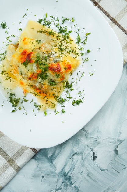 Gedeelte van zelfgemaakte Italiaanse lasagne met kaas, witte saus en kip op witte plaat met doek. Traditionele Italiaanse pasta. Grijze tafel