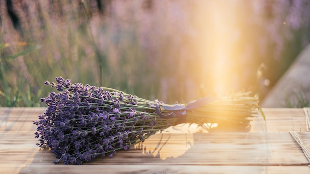 Gedeeltelijk wazig bosje lavendel op een houten bord tegen de achtergrond van struiken met bloemen en zonnestralen