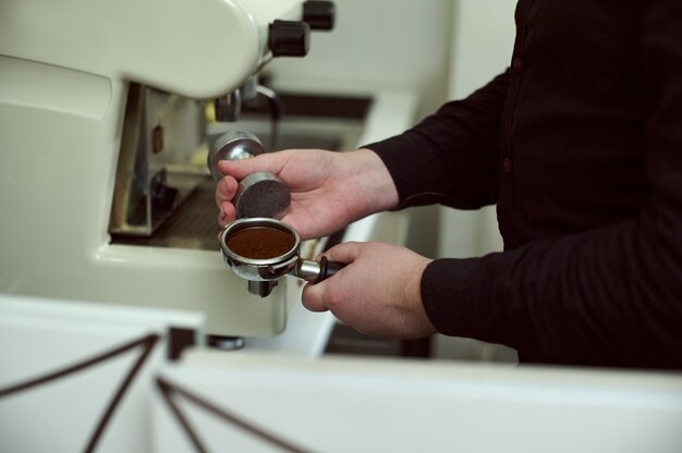 Gedeeltelijke weergave van barista in zwart shirt portafilter met gemalen koffie en stamper te houden