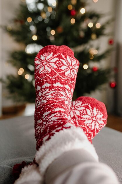 Gedeeltelijke weergave van voeten in kleurrijke wollen sokken tegen de achtergrond van een kerstboom