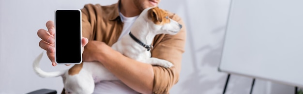 Gedeeltelijke weergave van zakenman die smartphone met leeg scherm toont terwijl hij jack russell terrier vasthoudt