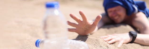 Gedehydrateerde man die op zand kruipt voor een fles drinkwater close-up