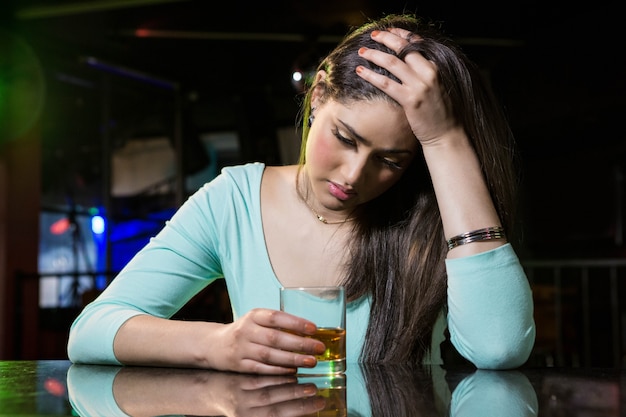 Gedeprimeerde vrouw die whisky hebben bij barteller in bar