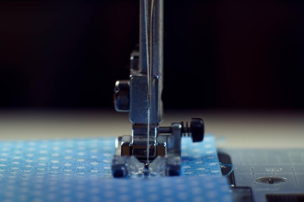 Gedetailleerd close-up shot van de stalen voet van de naaimachine met naald en draad stiksels op blauwe stof polka dot textiel