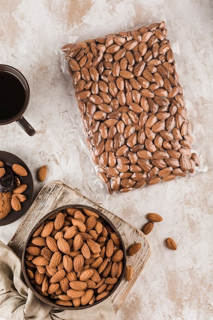 Gedroogde amandelen in een kom en in een vacuümverpakking met een kopje koffie op een lichte achtergrond. Een natuurlijk product voor de voeding. Bovenaanzicht met een kopie ruimte. Verticale oriëntatie.