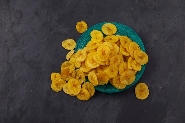 Gedroogde bananenchips of bananenwafels verspreid over een groene ronde basis met grijze achtergrond