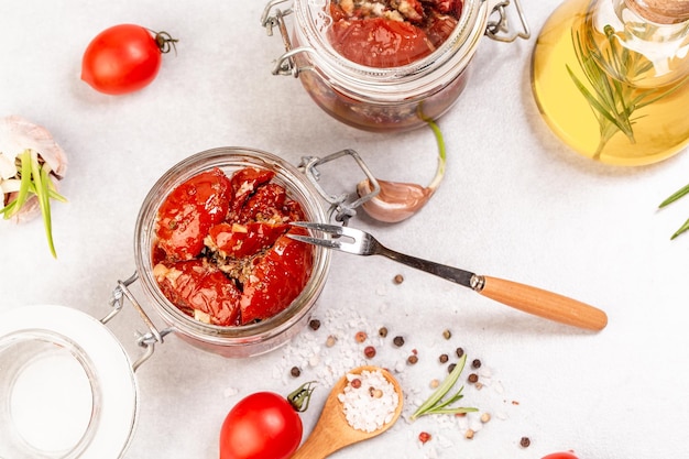 Gedroogde gedroogde rode tomaten met kruiden bovenop in een kleine pot. Heerlijke snack op een lichte achtergrond, bovenaanzicht.