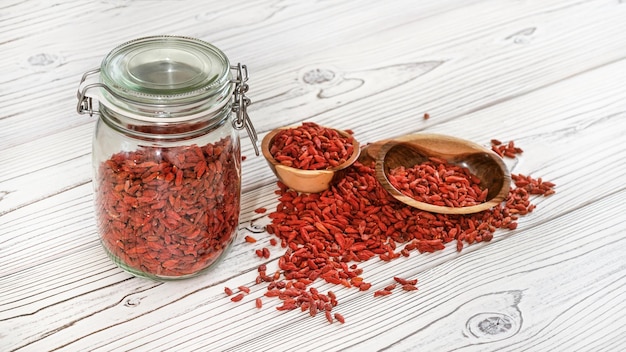 Gedroogde goji aka. wolfberry-zaden in glazen fles, sommige in houten kommen en gemorst op een bureau met witte borden