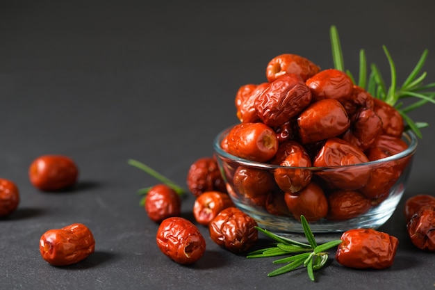 Gedroogde Jujube, Chinees gedroogd rood datafruit met rozemarijnblad in glaskop op zwarte achtergrond, kruidenvruchten.