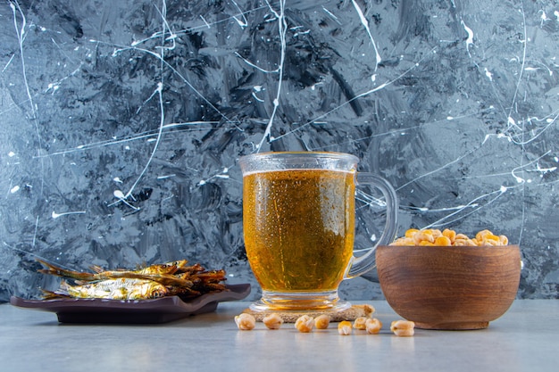 Gedroogde kleine gezouten sprot op een schotel naast bierglas en kikkererwten, op de marmeren achtergrond.