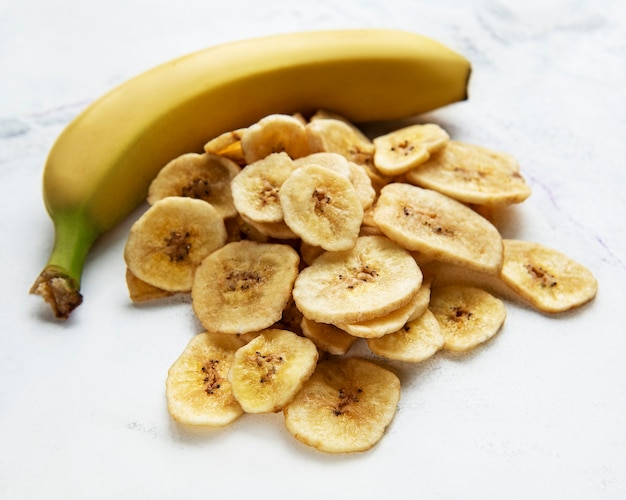 Gedroogde plakjes banaan of chips op een witte marmeren achtergrond