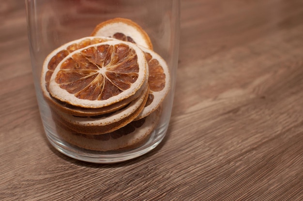 Gedroogde sinaasappelen in een glazen pot op een houten tafel met een plek voor tekst