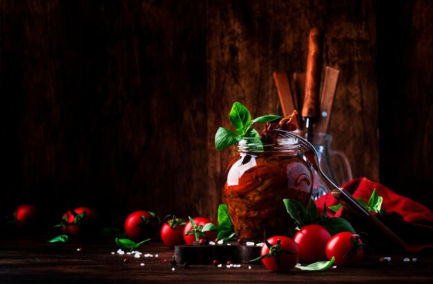 Gedroogde tomaten in olijfolie met groene basilicum en kruiden in glazen pot op houten keukentafel rustieke stijl plek voor tekst