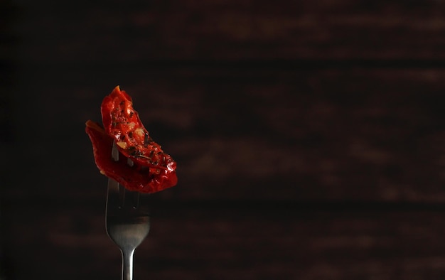 Gedroogde tomaten met Italiaanse kruiden op een vork op een donkere achtergrond
