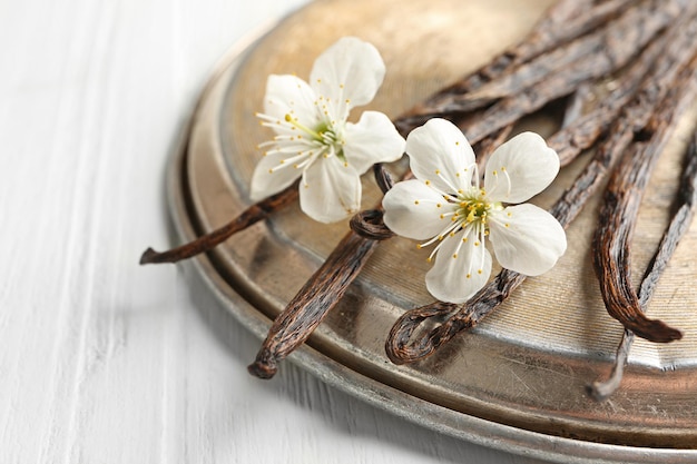 Gedroogde vanillestokjes bloemen en metalen plaat op lichte houten close-up als achtergrond