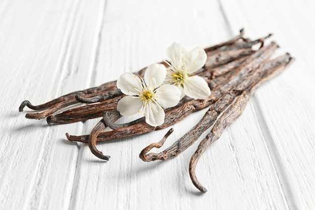 Gedroogde vanillestokjes en bloemen op lichte houten close-up als achtergrond