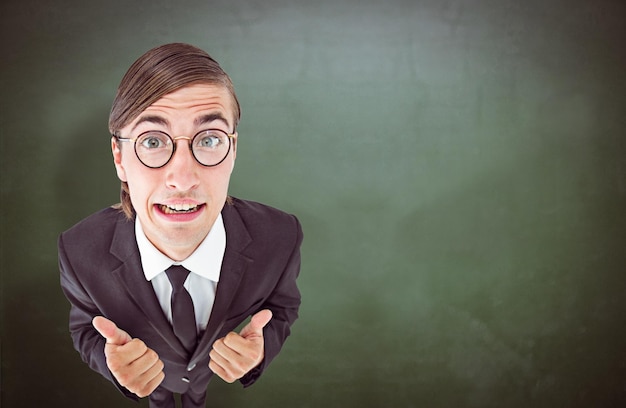 Geeky businessman looking at camera thumbs up  against green chalkboard