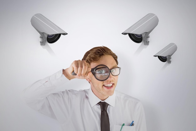 Geeky businessman looking through magnifying glass against cctv camera
