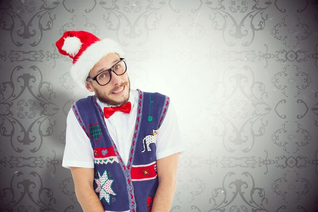 Geeky hipster in kerstmuts tegen elegant patroonbehang in grijstinten