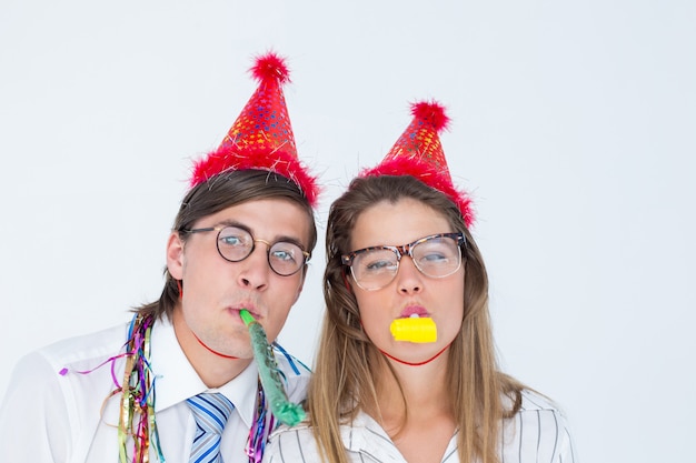 Geeky hipster wearing a party hat with blowing party horn