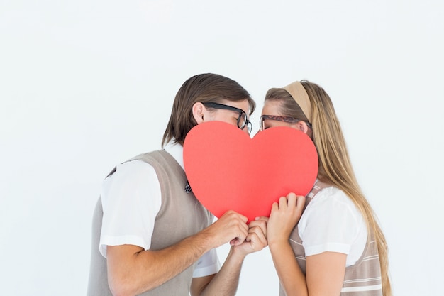 Geeky hipsters kissing behind heart card 