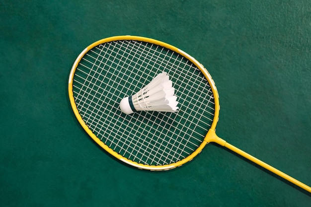 Geel badmintonracket en witte badmintonshuttle op groene vloer in indoor badmintonveld