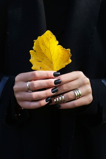 Foto geel de herfstblad in vrouwelijke handen met zwarte manicure