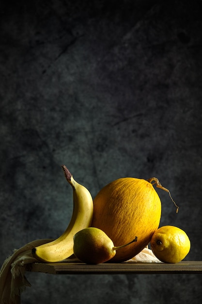Geel fruit op een zwarte achtergrond, meloen, banaan, peer, citroen, op een houten tafel, creatief fruit