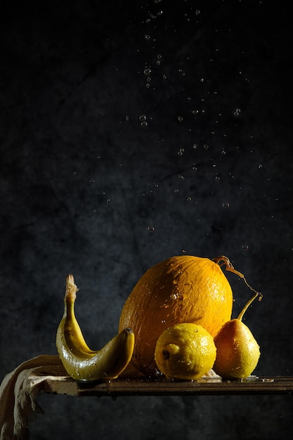 Geel fruit op een zwarte achtergrond, meloen, banaan, peer, citroen, op een houten tafel, creatief fruit