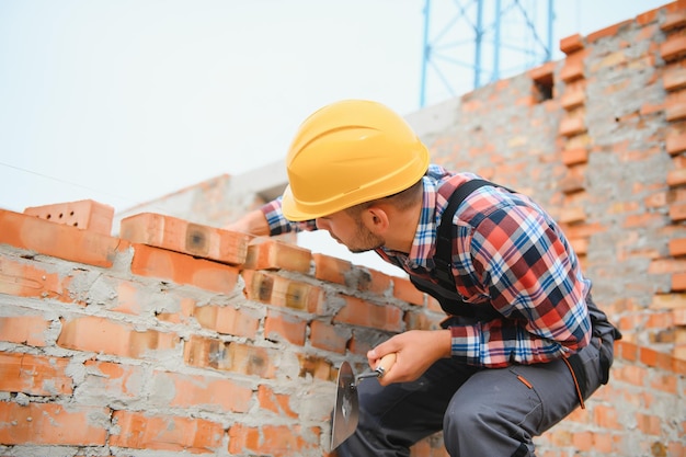 Geel gekleurde helm Jonge man aan het werk in uniform in de bouw overdag